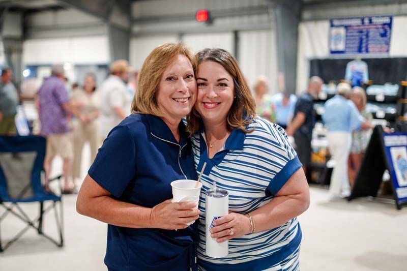 Two women smiling and holding drinks in a busy indoor venue