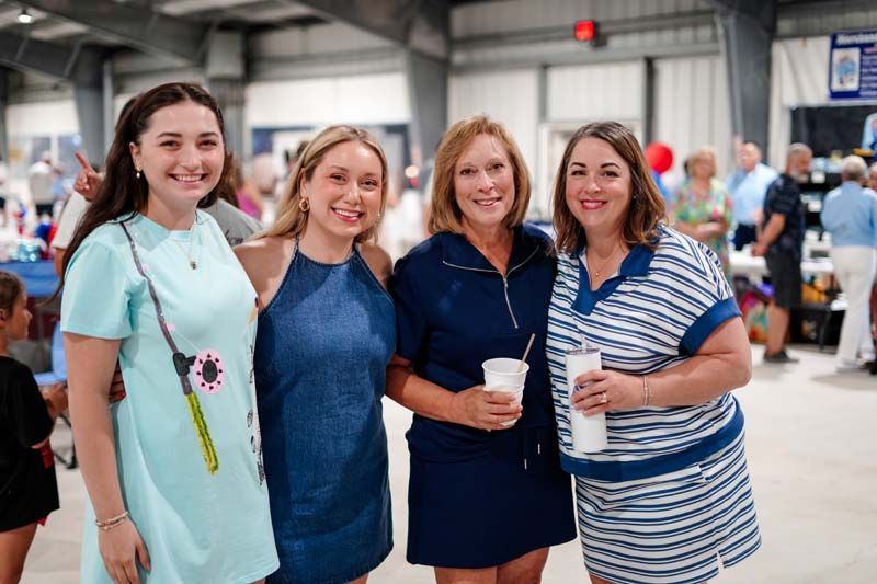 Four women smiling at an indoor event, standing together with drinks.