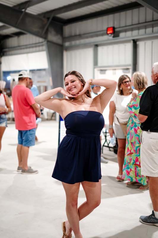 Woman in a navy dress posing with hands behind her head at an indoor social event