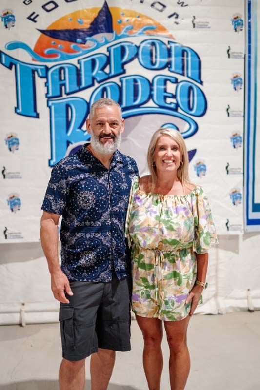 Two people posing in front of a Tarpon Rodeo banner at an indoor event