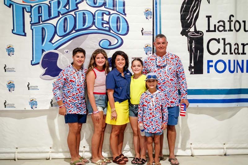 Six people posing in matching shirts at the Tarpon Rodeo event backdrop