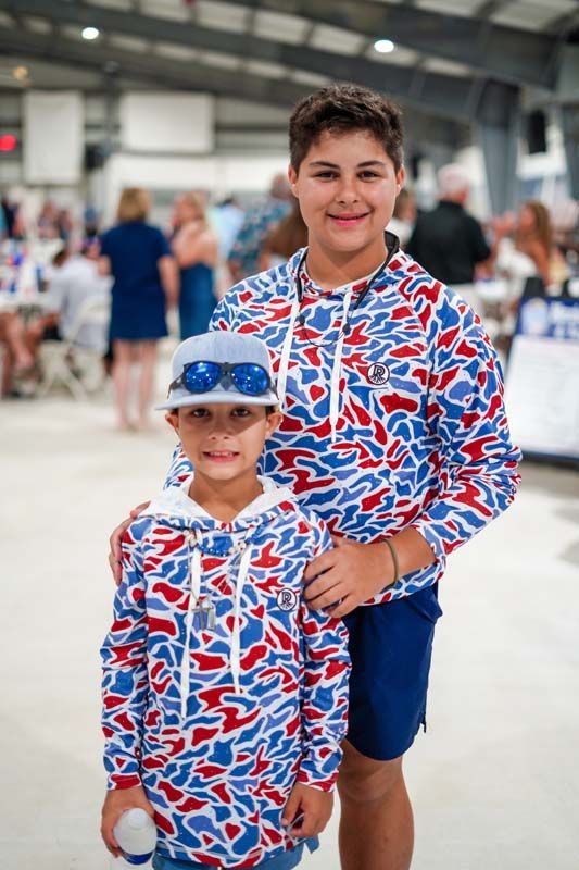 Two people in matching red, white, and blue shirts posing in a busy indoor venue