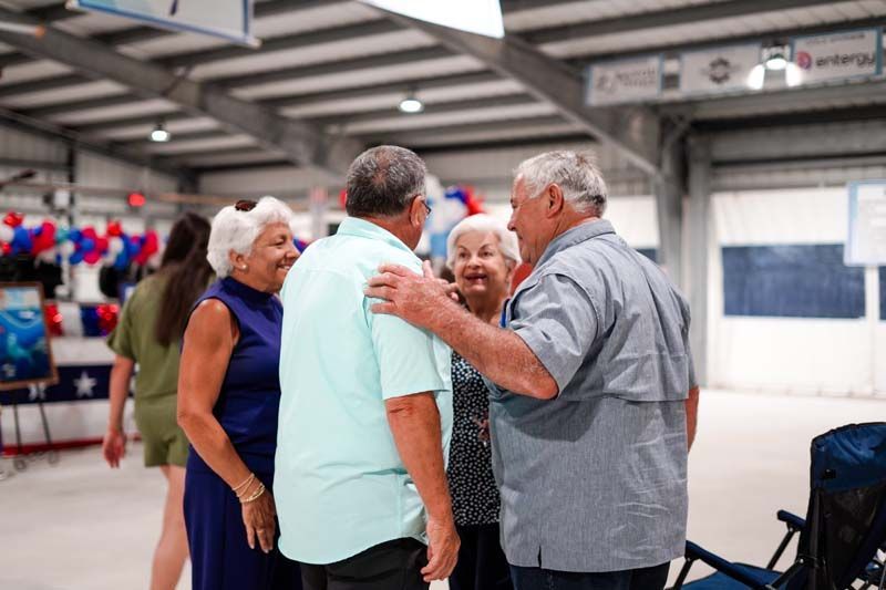 Four people chatting and smiling in a bright indoor hall, with balloons in the background.