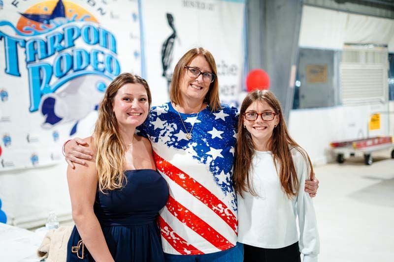 Three people smiling indoors, with one wearing an American flag shirt.