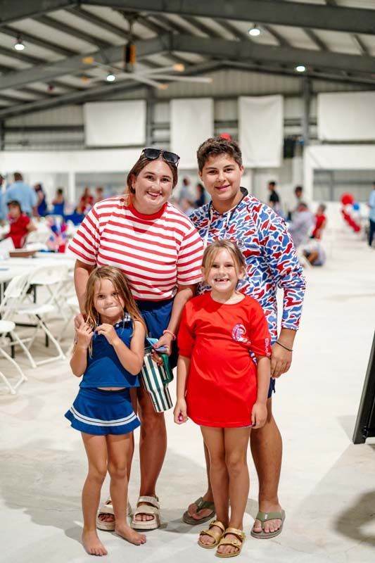 Two adults and two children posing indoors on a sports court, smiling and wearing red, white, and blue outfits