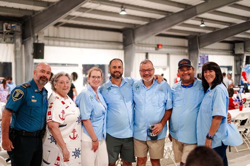 Six people standing together indoors, smiling in light blue shirts at a ceremony