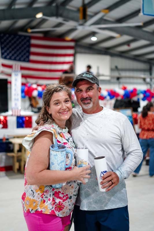 Two people smiling at an indoor event with an American flag in the background