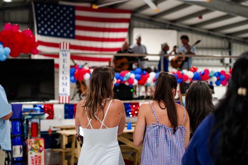 People watching a stage decorated with red, white, and blue balloons and a large American flag