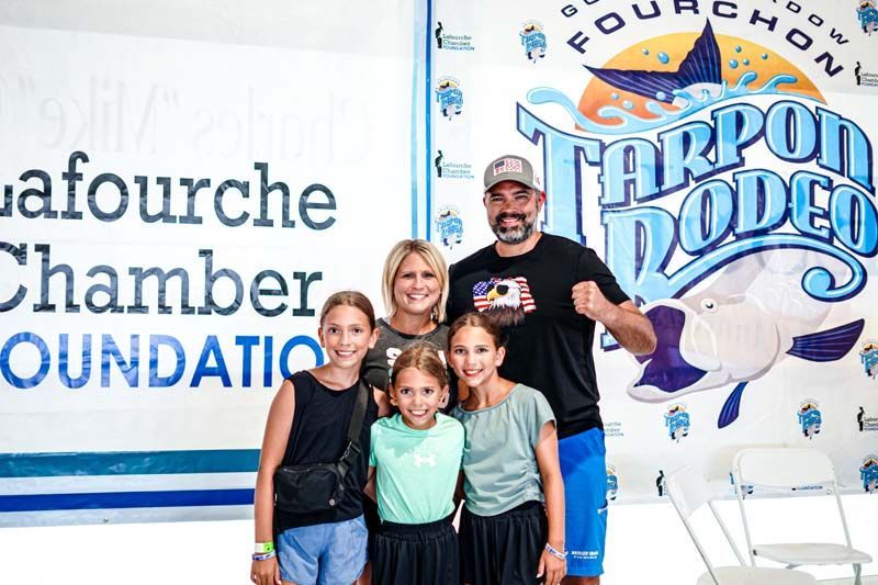 A family is posing for a picture in front of a tarpon rodeo sign.