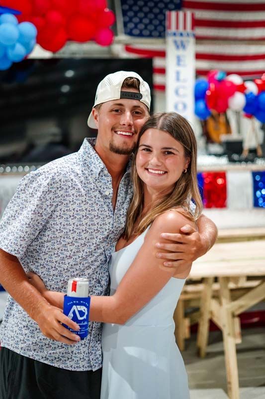 Smiling couple posing together at a patriotic indoor event with red, white, and blue decorations.