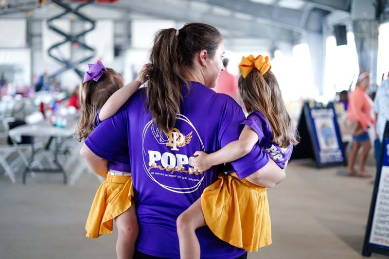 Two people in purple shirts carrying yellow Pom Poms at a covered sports venue