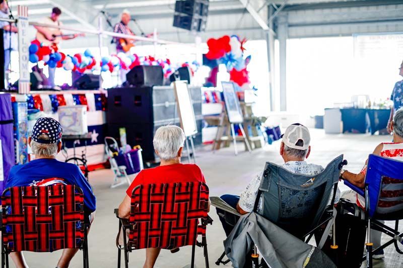 People seated in folding chairs watching a decorated indoor event stage and ladder setup