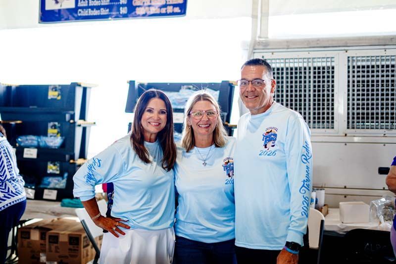 Three people in matching light blue shirts smiling indoors at a work table