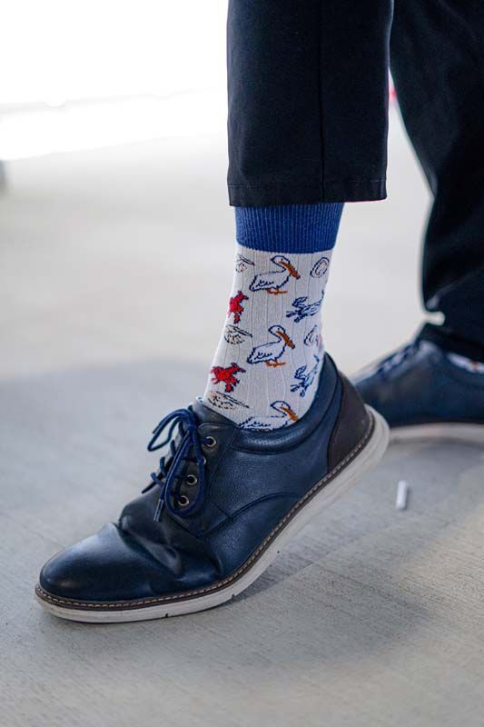 Close-up of a navy shoe and white patterned sock stepping on a gray floor.
