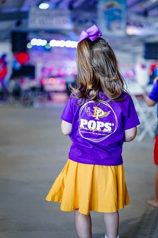 Child in a purple shirt with a bow and yellow skirt standing in a stadium concourse.