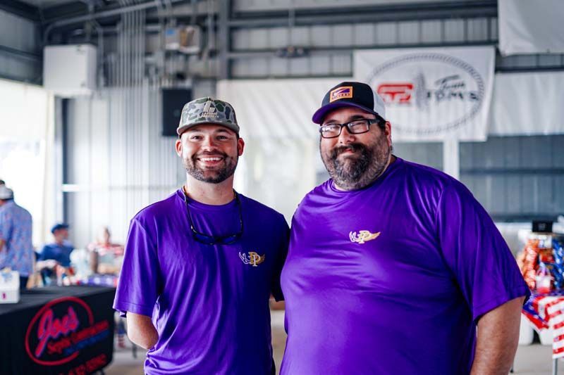 Two smiling men in purple shirts standing in an indoor event space