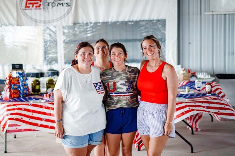 Three people pose in front of a red, white, and blue decorated table at an indoor event.