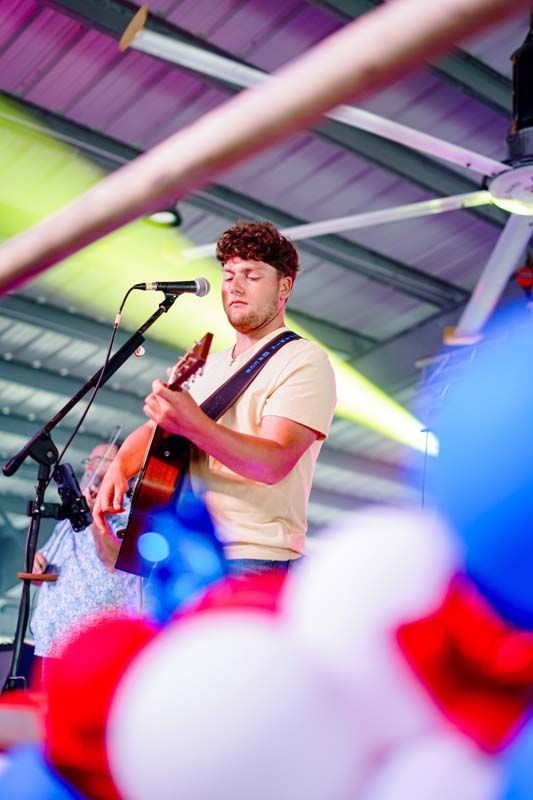 Musician playing guitar and singing on stage under colorful lights