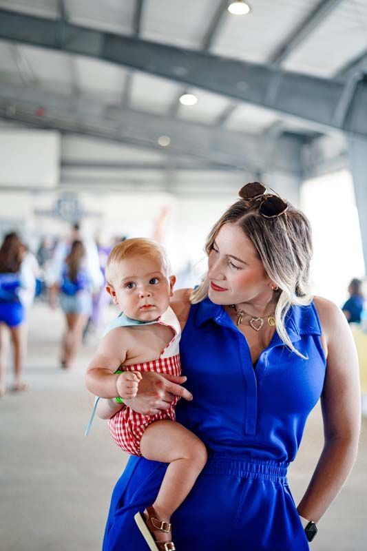 Woman in a blue dress holding a baby in a red polka-dot outfit indoors