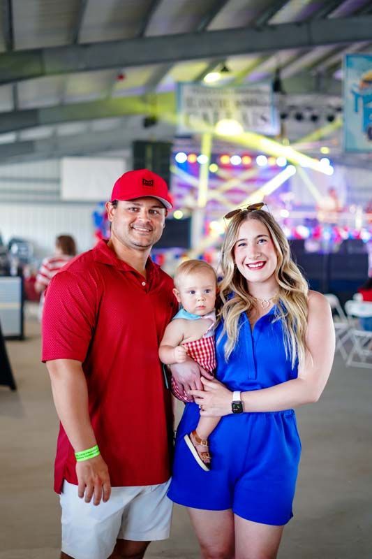 Three people standing together indoors, smiling, with colorful lights in the background.