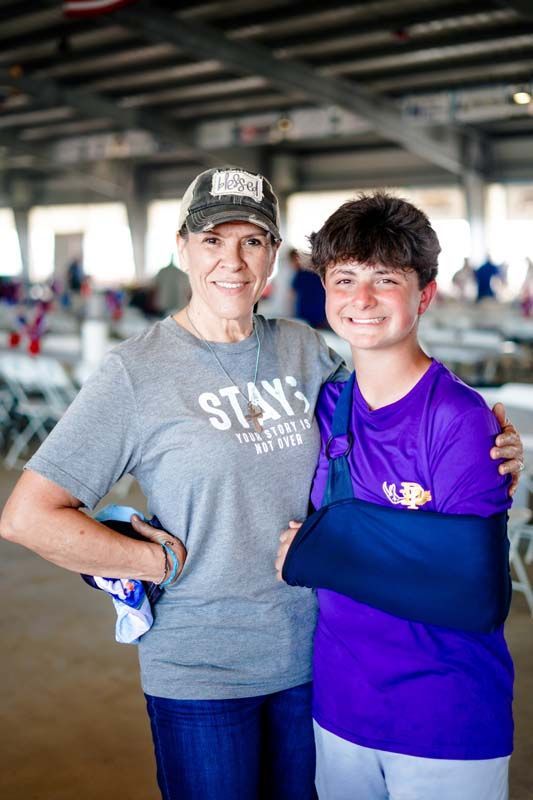 Two people smiling and hugging in a gym, wearing gray and purple shirts.