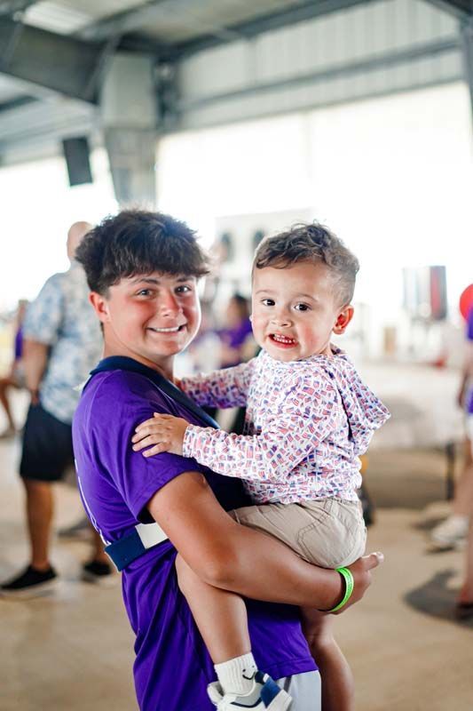 Two children smiling and being held indoors, one in a purple shirt and the other in a patterned top