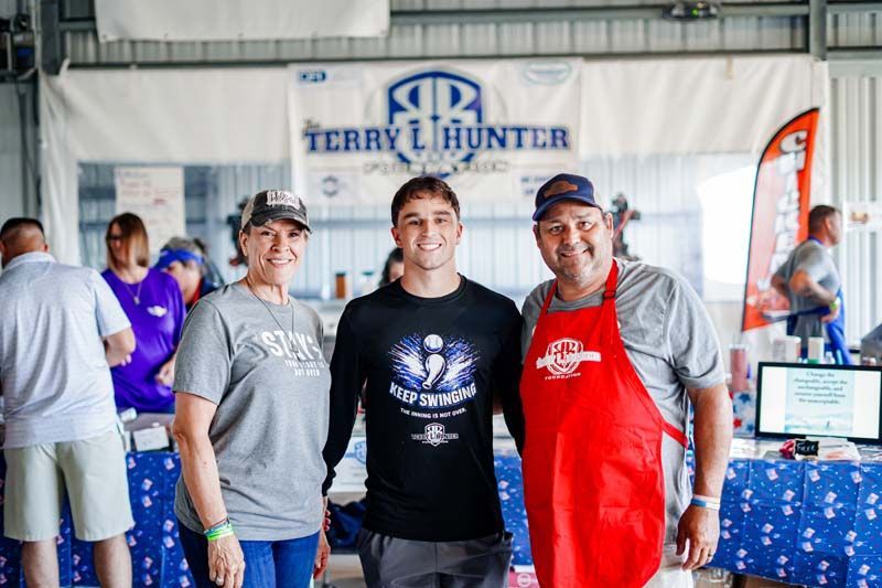 Three people posing at an indoor event booth with a Terry Hunter banner and table display behind them.