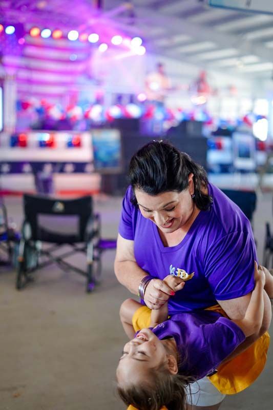 Two performers in purple and gold dance in a bright indoor venue, one dipping the other.