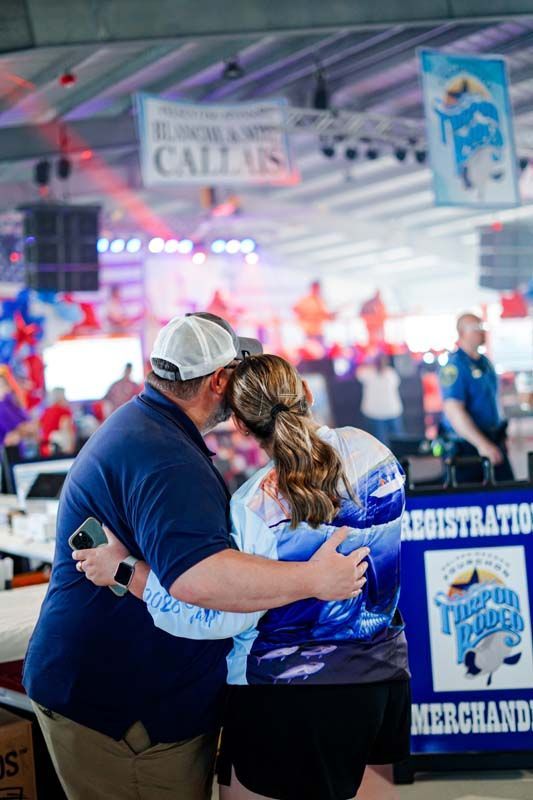 Couple embracing in a crowded indoor event booth with blue signage and bright lights