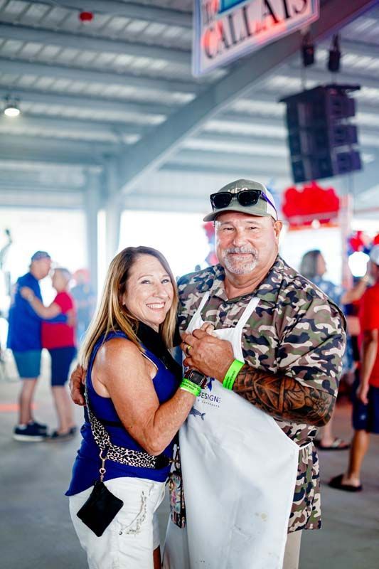 Two people smiling and posing together at an indoor event, one holding a drink and a white bag.