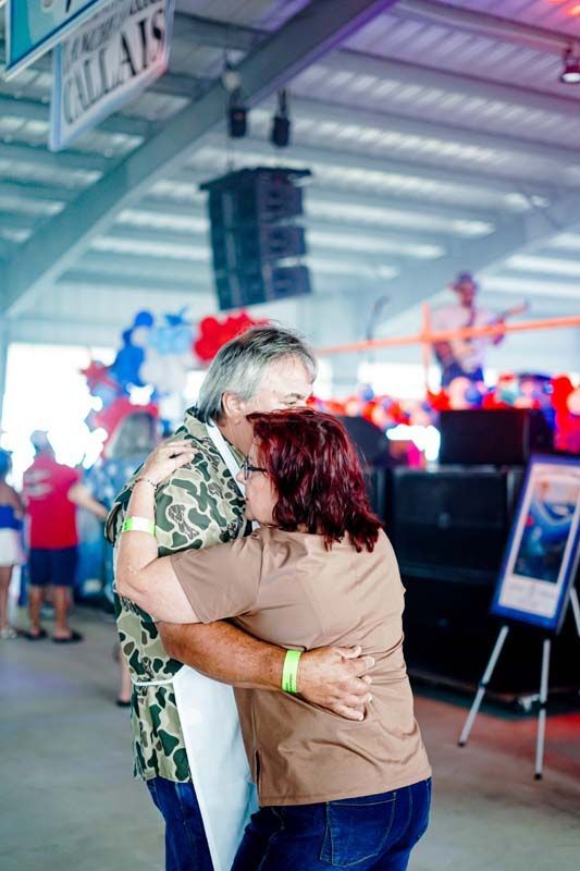 Two people hugging in a brightly lit indoor event space with red and blue decorations