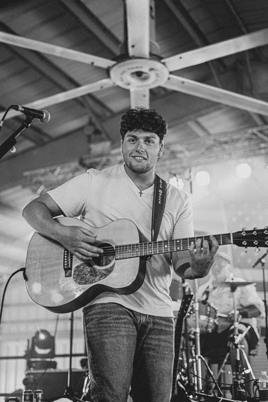 Musician singing and playing acoustic guitar on stage under a wooden pavilion ceiling