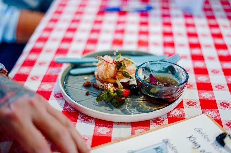 Colorful plated dessert on a blue plate beside a small bowl on a red-and-white checkered tablecloth