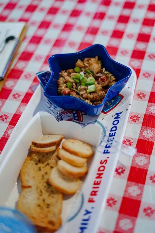 Blue bowl of mixed nuts with sliced bread on a red-and-white checkered tablecloth
