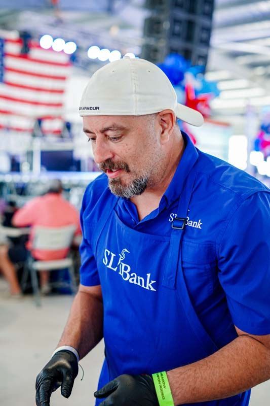 Man in blue shirt and gloves working at a bank event booth with U.S. flags in the background