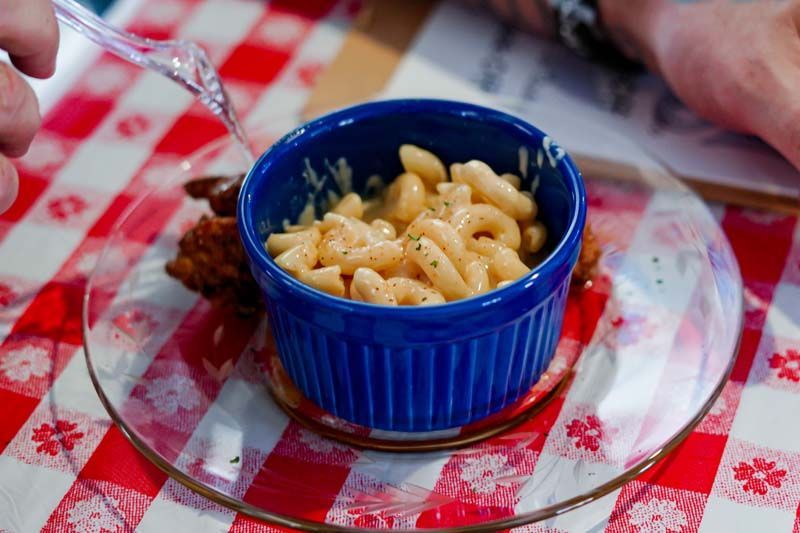 Blue bowl of macaroni on a red-and-white checkered tablecloth with a spoon beside it