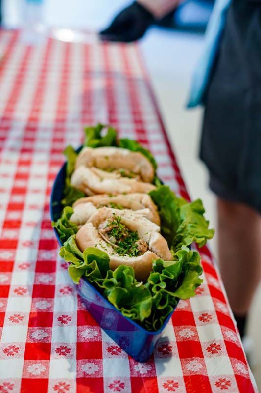 Three sandwiches in blue wrappers on lettuce-lined trays at a red-and-white checkered table