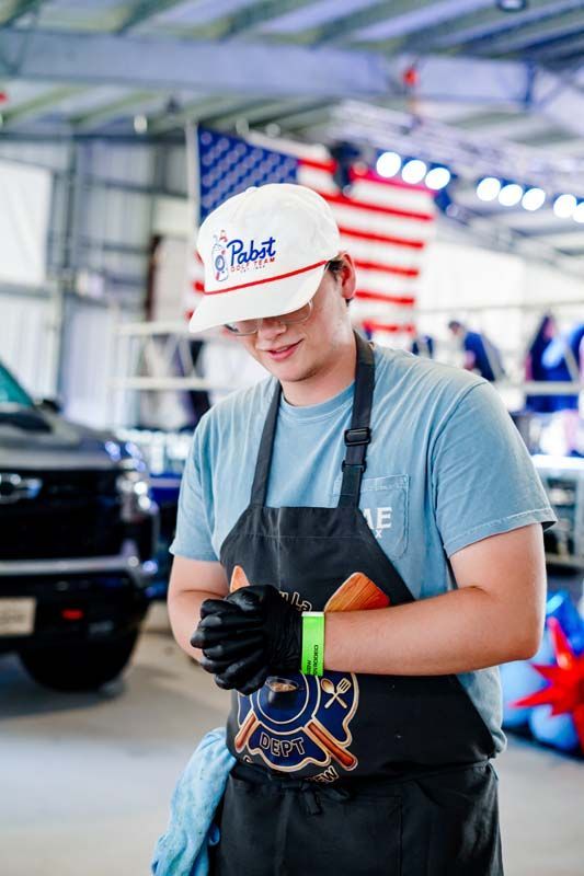 Worker in hard hat and gloves standing in a garage with a car and American flag backdrop