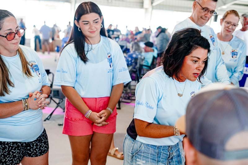 Group of volunteers in white T-shirts and bright shorts listening attentively at an outdoor event