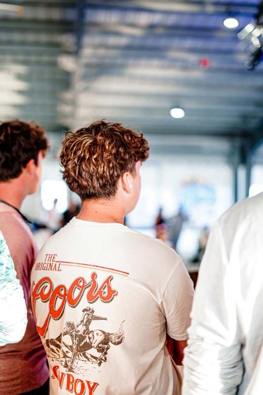 A man wearing a coors light shirt is standing in a crowd of people.