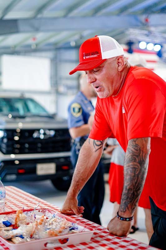 Man in red shirt and cap leaning over a table of packaged items at an indoor event