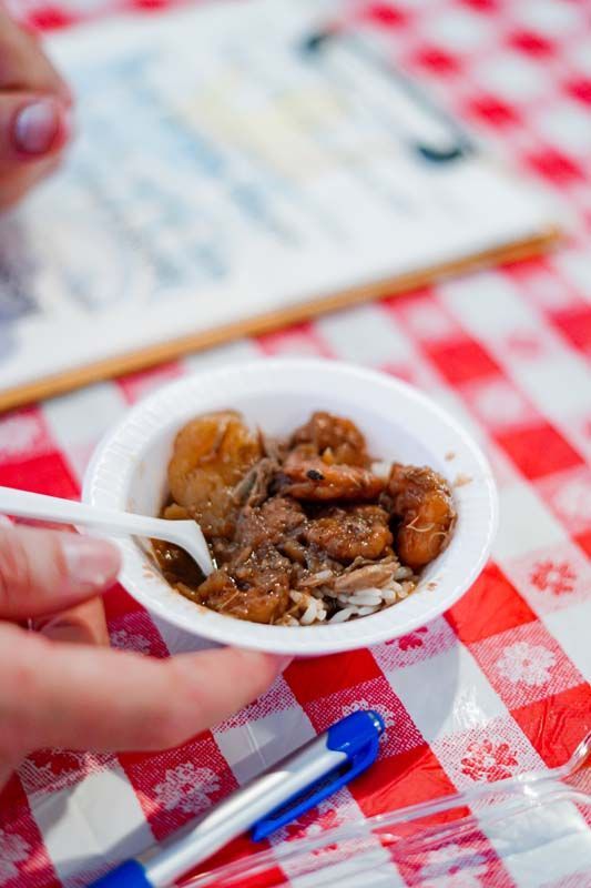 Hand holding a white spoonful of food over a red-and-white checkered tablecloth