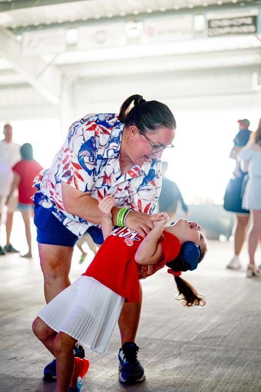 Adult guiding a child in a red dress through a dance move indoors