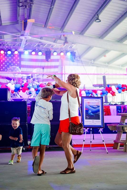 Woman and child dancing in a brightly lit indoor event hall with colorful stage lights and audience in background