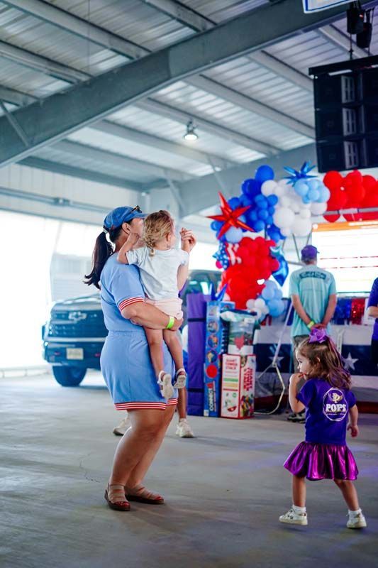 Woman holding child near red, white, and blue balloons in a warehouse event space