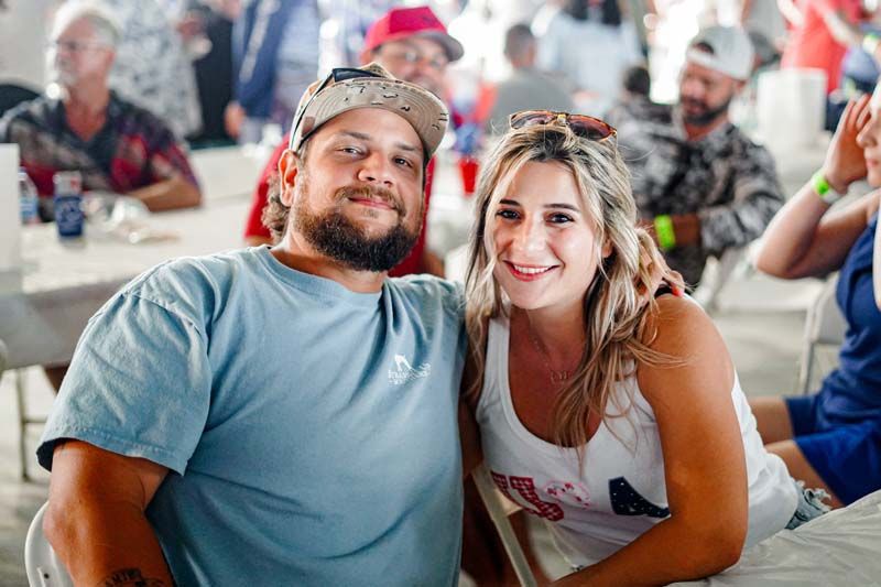 Smiling couple leaning together at a crowded outdoor event, with people blurred in the background