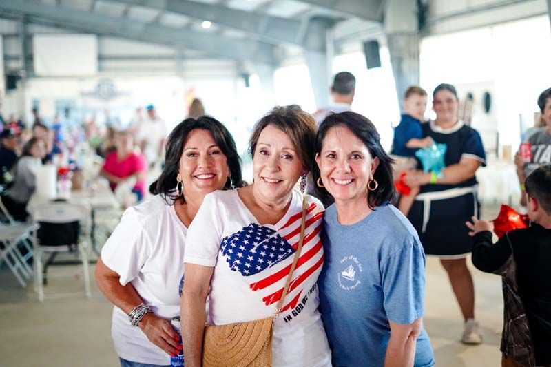 Three people smiling in a bright indoor hall, with one wearing an American flag shirt.