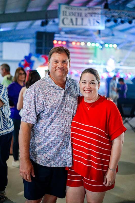 Two people smiling at an outdoor event, with colorful lights and a banner in the background