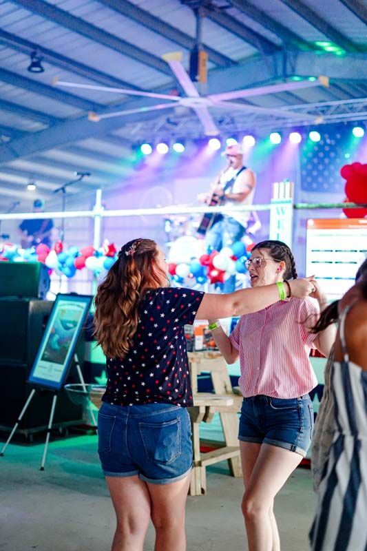 People dancing in a colorful indoor venue with stage lights and a large screen in the background