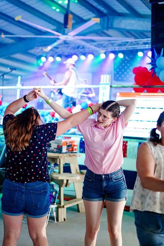 People dancing in a colorful indoor venue with stage lights and bunting overhead